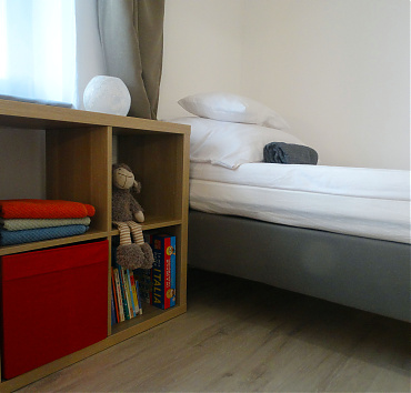 Gyerekkönyvek - Egyik ágy a háromágyas szobában, gyerekjátékokkal és mesekönyvekkel.